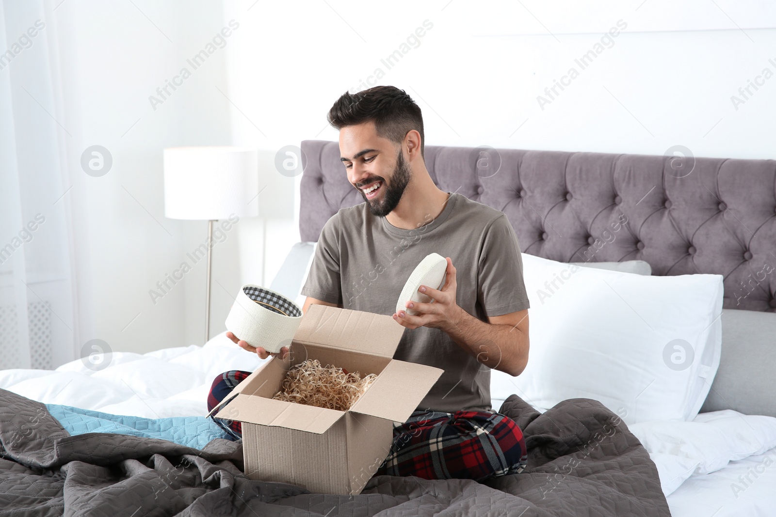 Photo of Young man opening parcel in bedroom at home