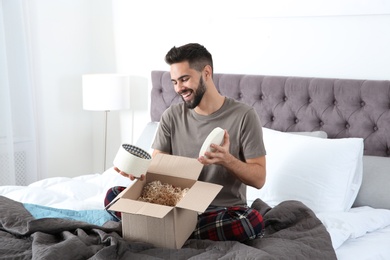 Young man opening parcel in bedroom at home