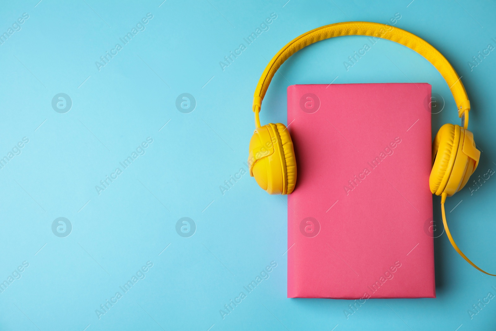 Photo of Book and headphones on light blue background, flat lay. Space for text