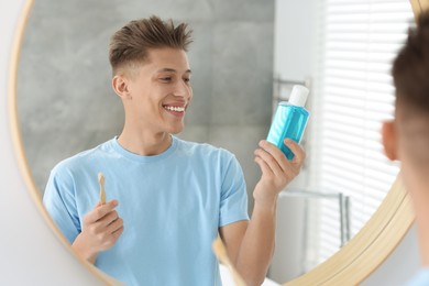 Photo of Young man with mouthwash and toothbrush near mirror in bathroom