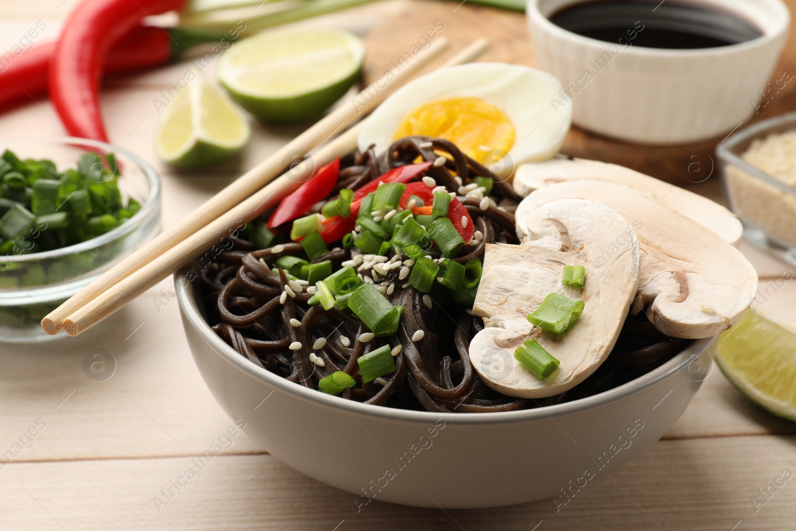 Photo of Tasty buckwheat noodles (soba) with mushrooms, onion, chili pepper, egg and chopsticks on wooden table, closeup