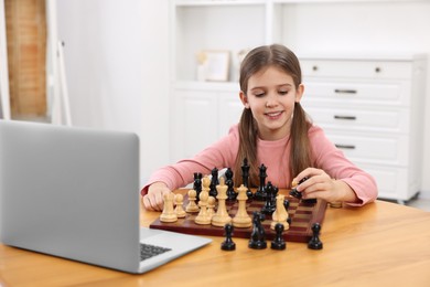 Cute girl learning to play chess with online tutor at home