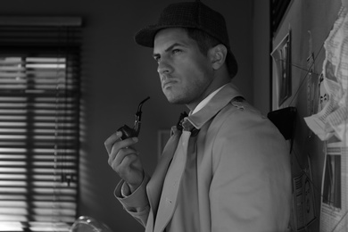 Photo of Old fashioned detective with smoking pipe near investigation board in office. Black and white effect