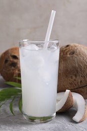 Photo of Glass of coconut water with ice cubes, palm leaf and nuts on grey table