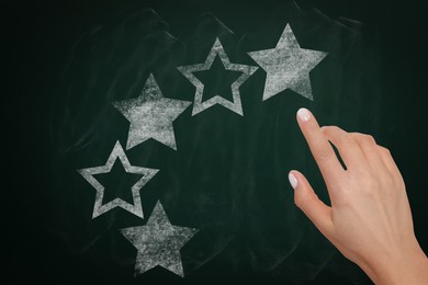 Image of Quality rating. Woman pointing at stars on chalkboard, closeup