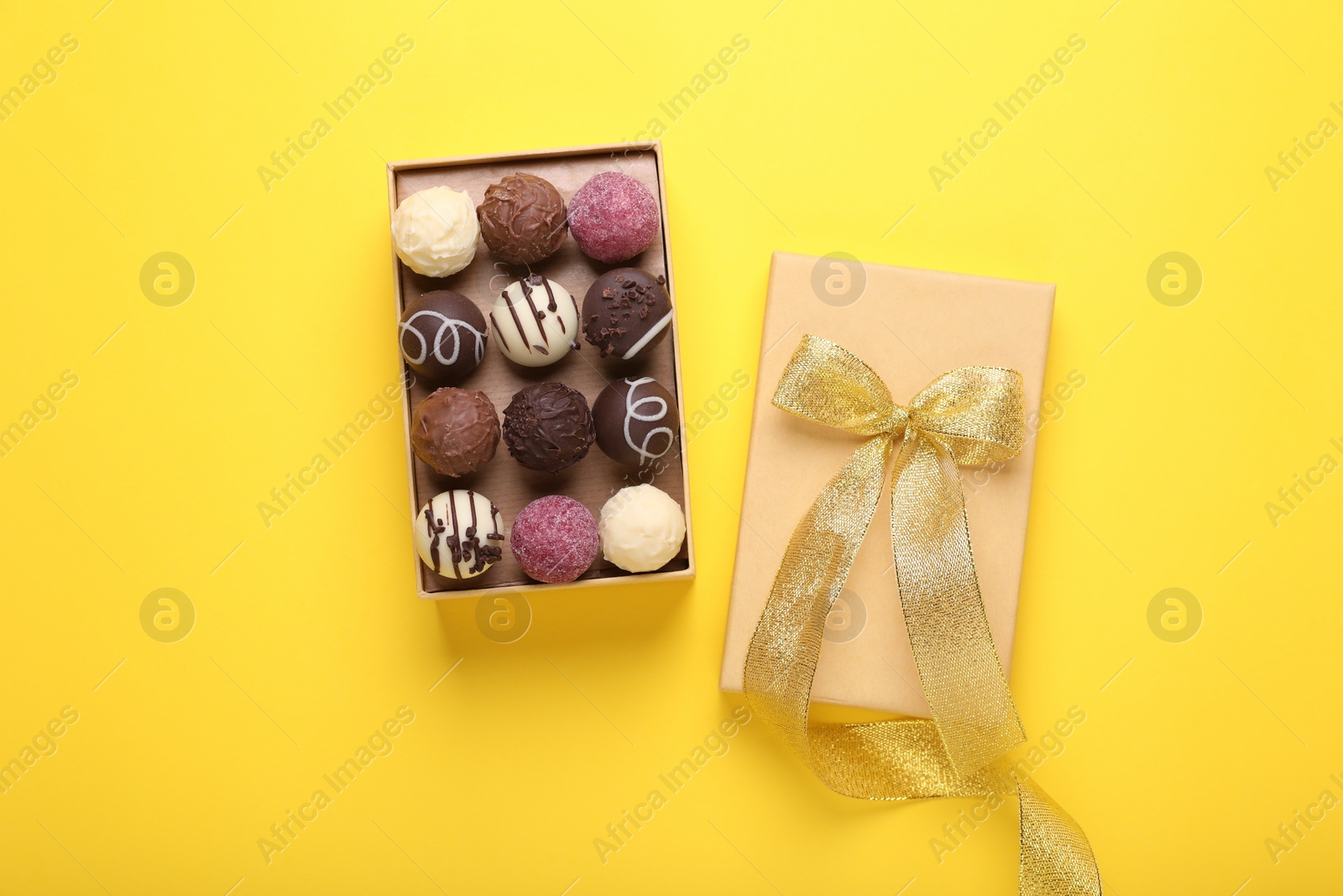 Photo of Open box with delicious chocolate candies on yellow background, top view