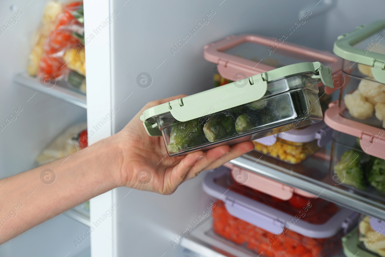 Photo of Woman taking container with frozen brussels sprouts from refrigerator, closeup