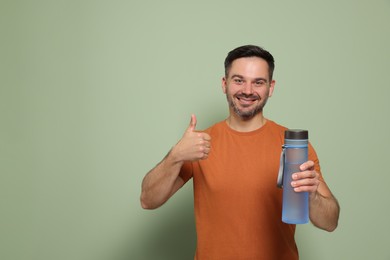 Photo of Happy man holding transparent bottle of water and showing thumb up on light green background, space for text