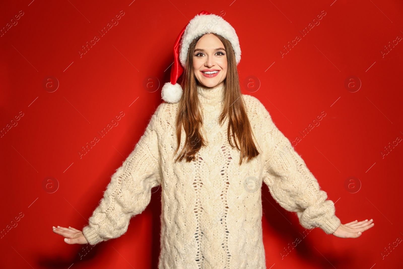 Photo of Young woman in Christmas sweater and Santa hat on red background