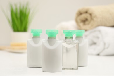 Photo of Mini bottles of cosmetic products on white table against blurred background