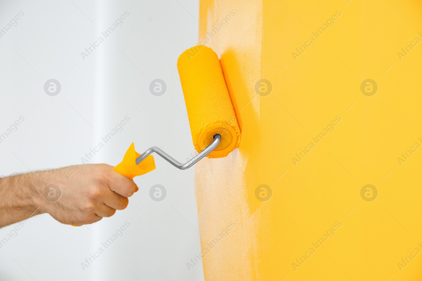 Photo of Man painting white wall with yellow dye, closeup. Interior renovation