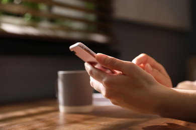 Photo of Woman with smartphone at table indoors, closeup on hands
