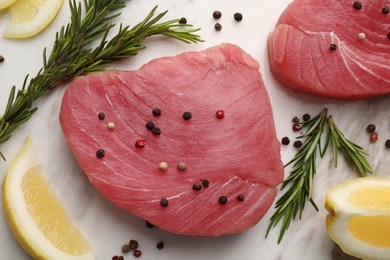 Photo of Raw tuna fillets with peppercorns, lemon and rosemary on white table, flat lay