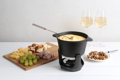 Fondue pot with tasty melted cheese, forks, wine and different snacks on white wooden table