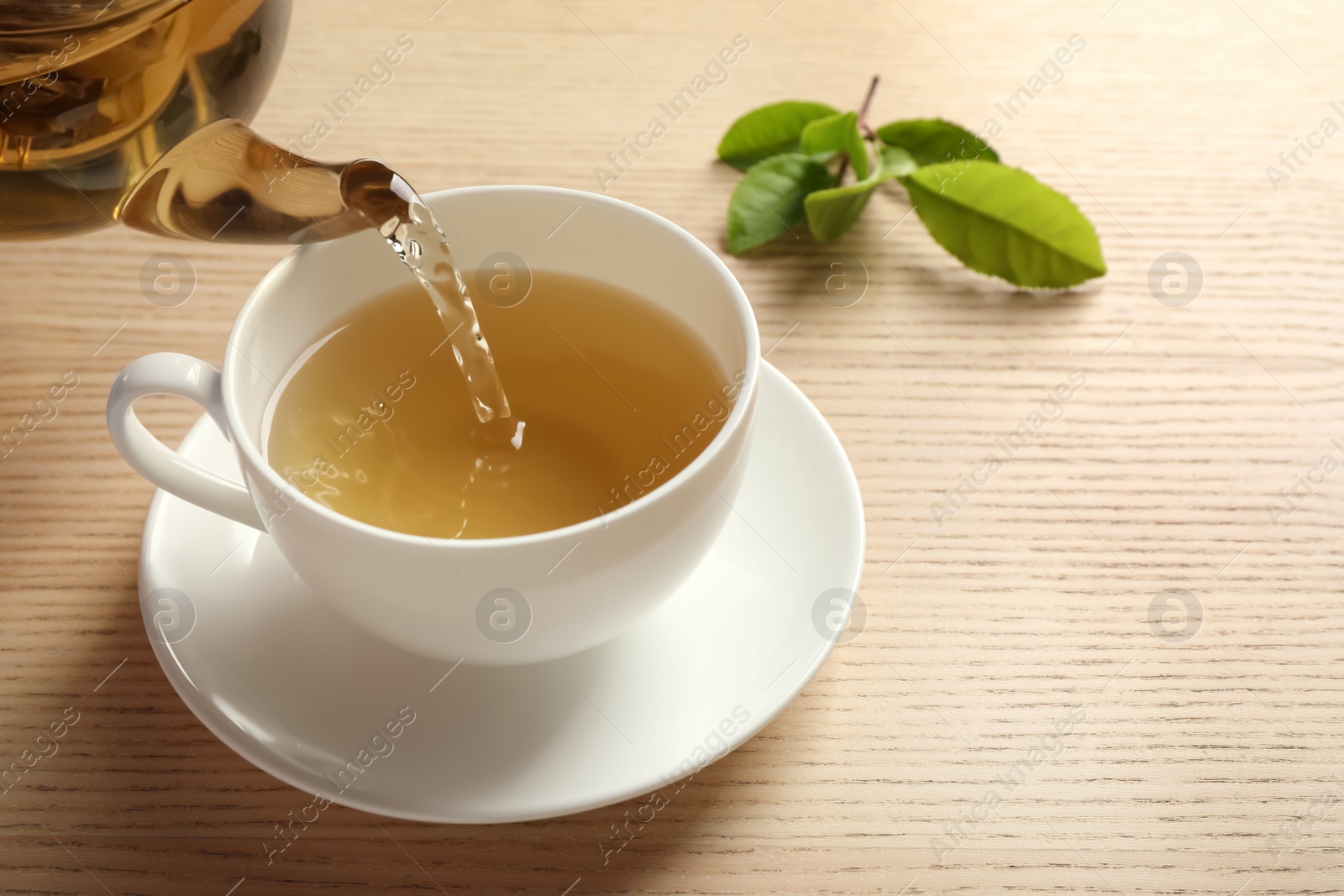 Photo of Pouring green tea into cup on wooden table. Space for text