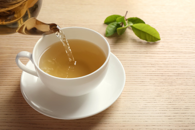 Photo of Pouring green tea into cup on wooden table. Space for text