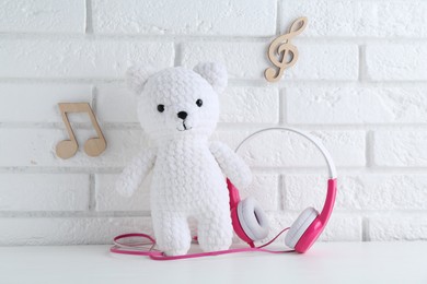Photo of Baby songs. Toy bear and headphones on white wooden table and notes