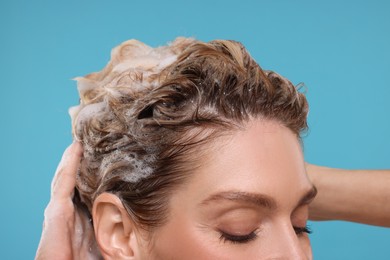 Photo of Woman washing hair on light blue background, closeup