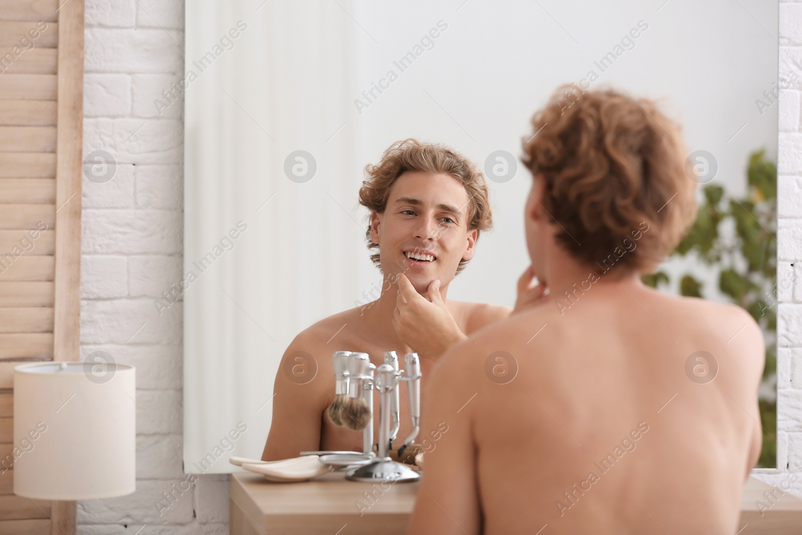 Photo of Young man looking in mirror after shaving at home