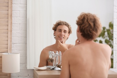 Photo of Young man looking in mirror after shaving at home