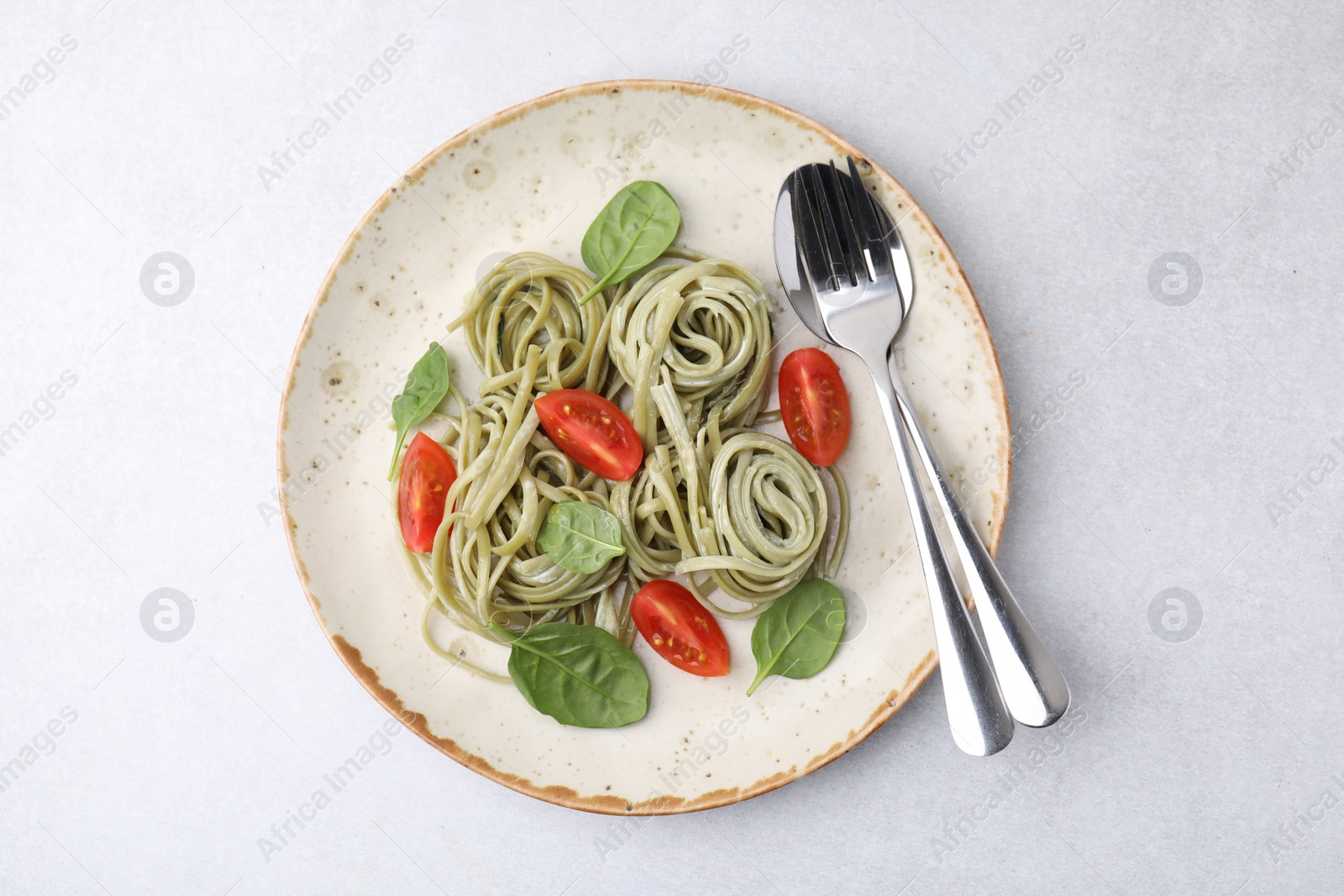 Photo of Tasty pasta with spinach, tomatoes and cutlery on light grey table, top view