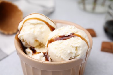 Photo of Scoopsice cream with caramel sauce and candies on light grey table, closeup