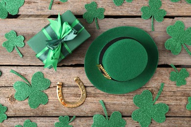 St. Patrick's day. Leprechaun hat, golden horseshoe, green gift box and decorative clover leaves on wooden background, flat lay