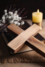 Cross, Bible, burning church candle and willow branches on wooden table, closeup