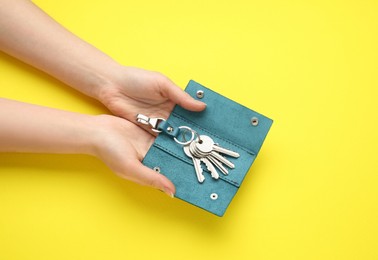 Woman holding open leather holder with keys on yellow background, top view