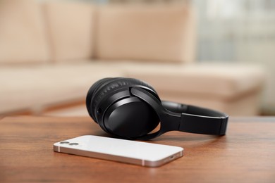 Photo of Modern wireless headphones and smartphone on wooden table indoors