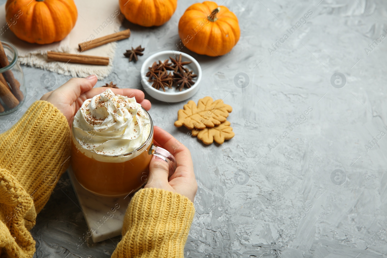 Photo of Woman holding cup of pumpkin spice latte with whipped cream at light grey table, closeup. Space for text