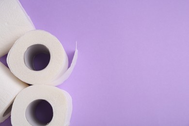 Photo of Soft toilet paper rolls on violet background, flat lay. Space for text