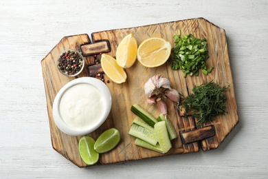 Photo of Board with cucumber sauce and ingredients on wooden background, top view