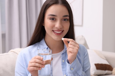 Photo of Beautiful young woman with glass of water and pill at home