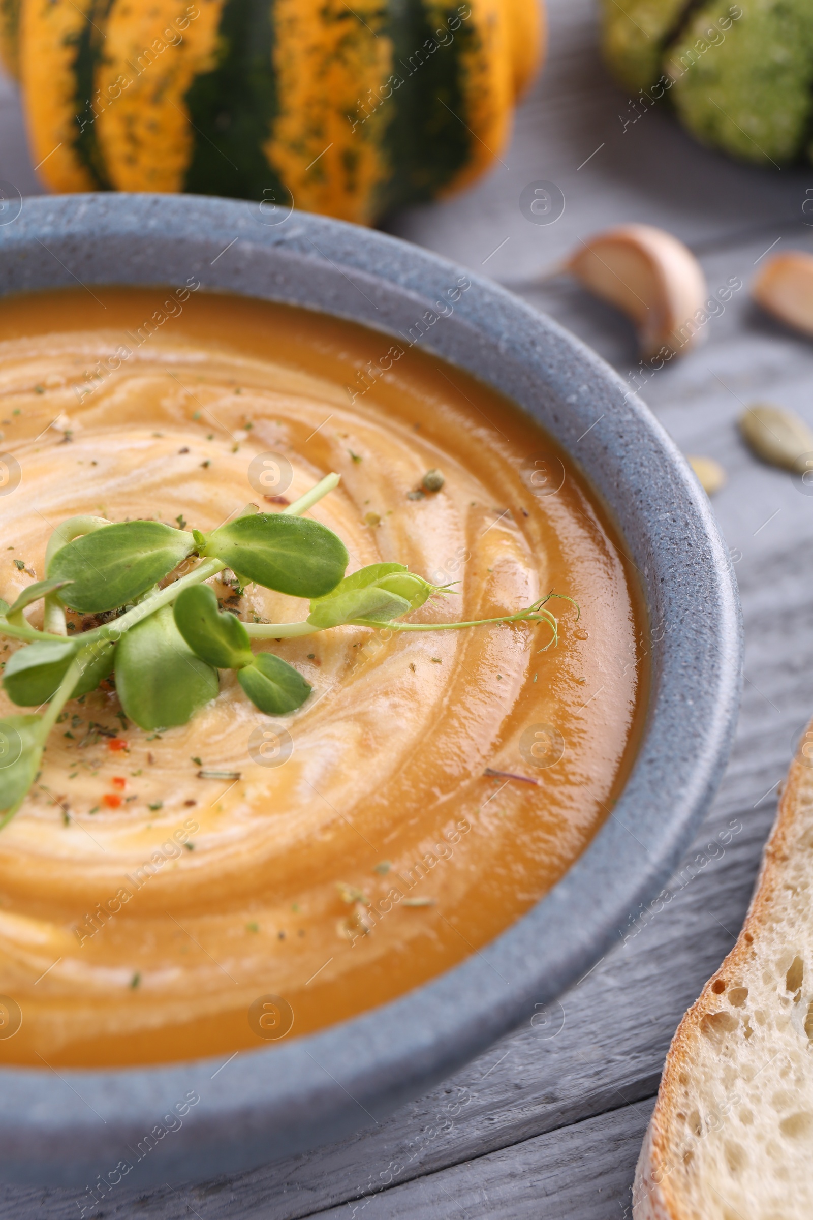 Photo of Tasty pumpkin soup with microgreens in bowl on grey wooden table, closeup