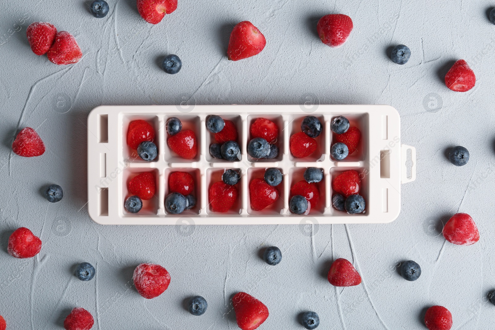 Photo of Flat lay composition with ice cube tray and berries on grey background