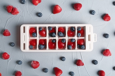 Photo of Flat lay composition with ice cube tray and berries on grey background