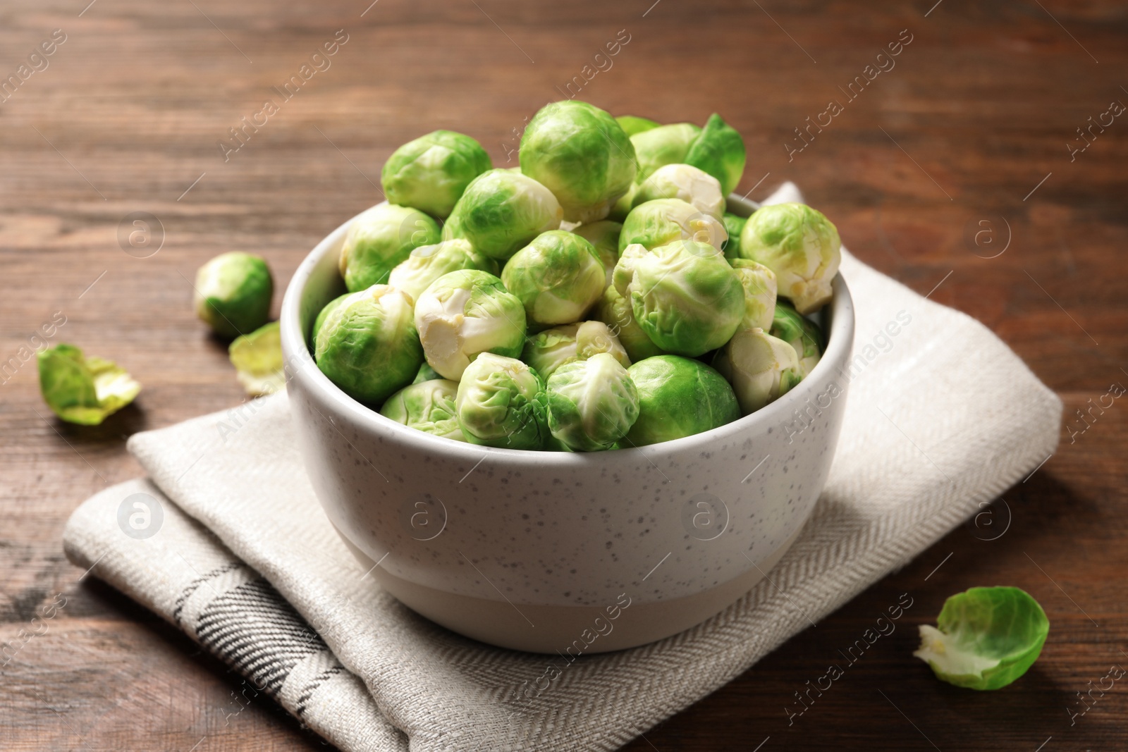 Photo of Bowl of fresh Brussels sprouts and napkin on wooden table