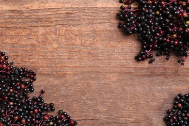Photo of Tasty elderberries (Sambucus) on wooden table, flat lay. Space for text
