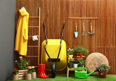 Gardening tools with wheelbarrow and flowers near wooden wall