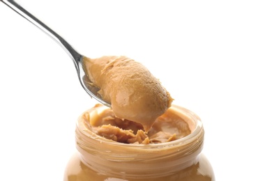 Photo of Spoon and jar with creamy peanut butter on white background