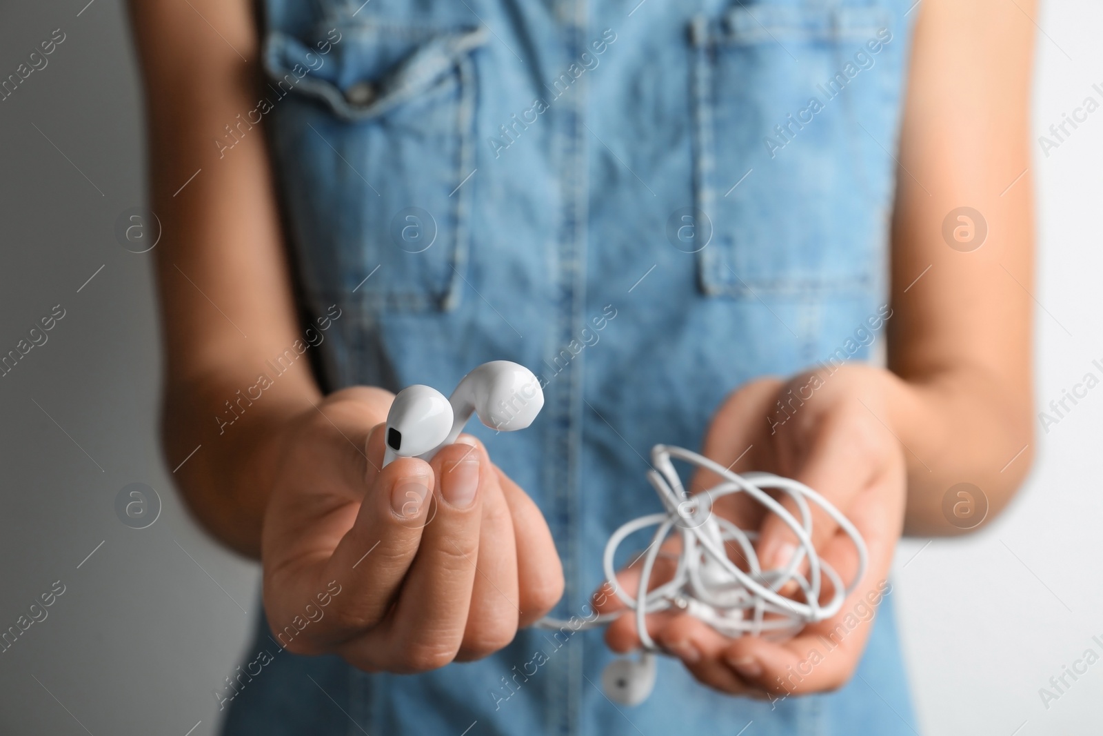 Photo of Woman holding different earphones on light background, closeup