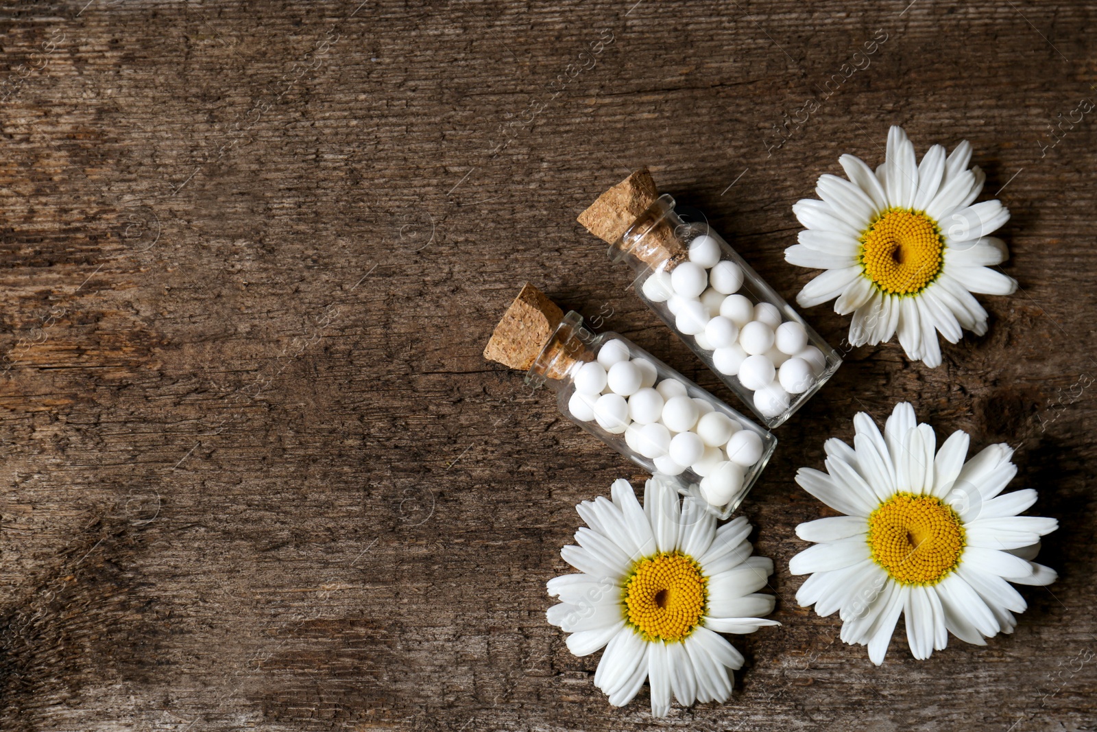 Photo of Bottles of homeopathic remedy and beautiful chamomiles on wooden background, flat lay. Space for text