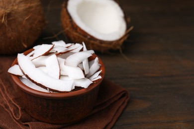 Photo of Coconut pieces in bowl and nuts on wooden table, space for text