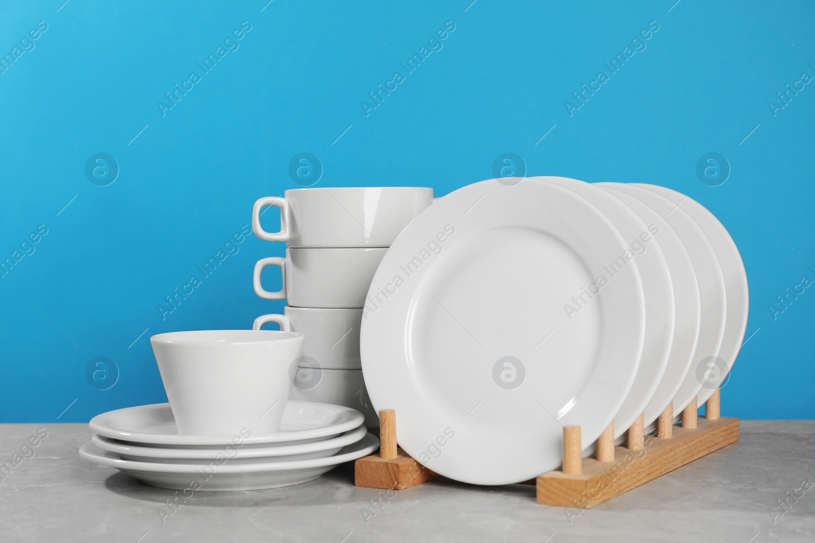 Photo of Set of clean tableware on grey table against light blue background