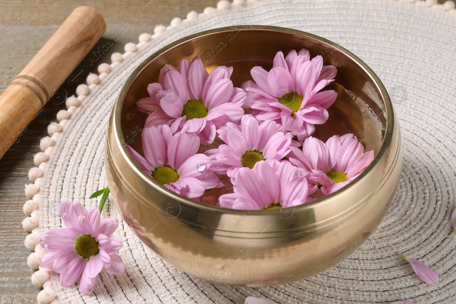 Photo of Tibetan singing bowl with water, beautiful flowers and mallet on wooden table, closeup