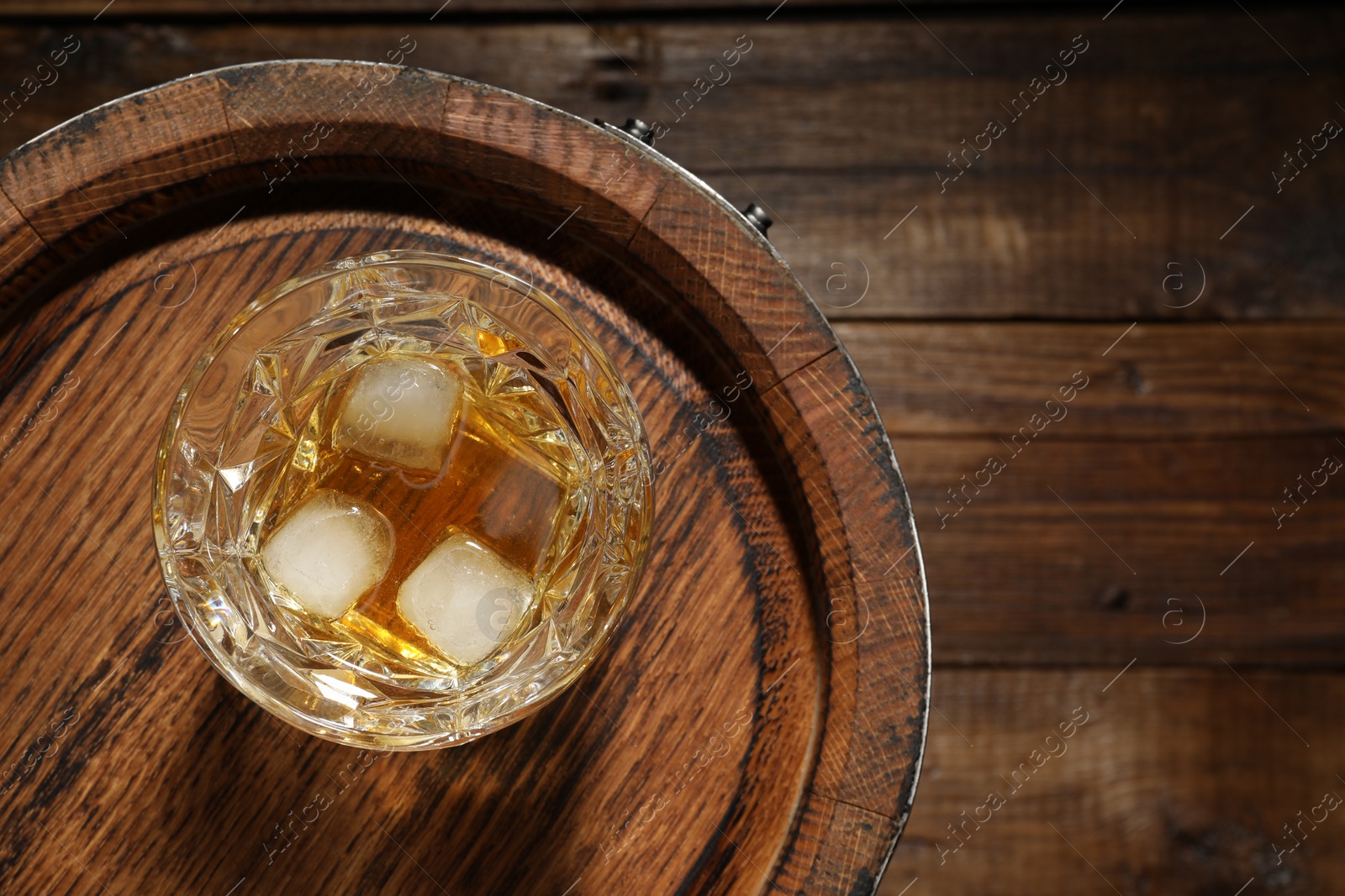 Photo of Glass of whiskey and barrel on wooden background, top view. Space for text