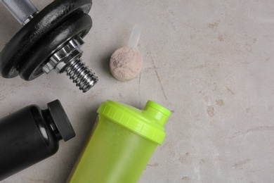 Bottle with protein shake, scoop of powder and dumbbell on grey background, top view. Space for text