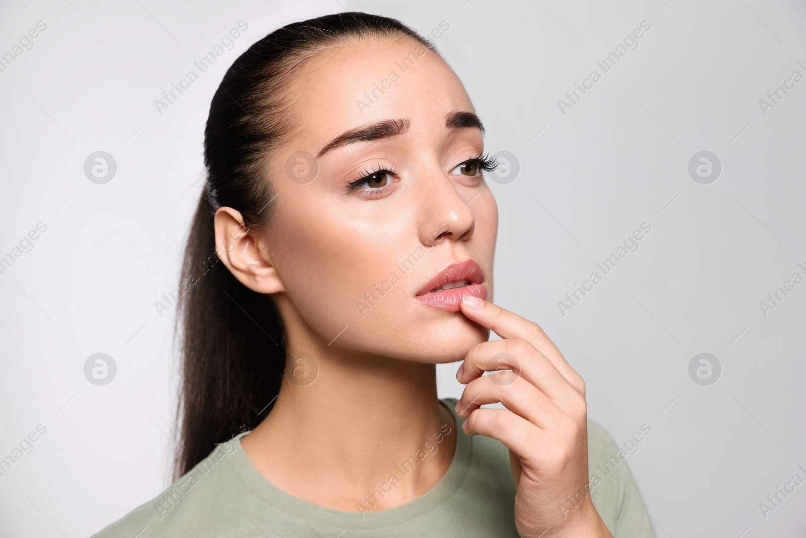 Photo of Woman with herpes touching lips on light grey background