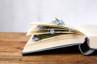 Beautiful forget-me-not flowers and book on wooden table against light background, closeup